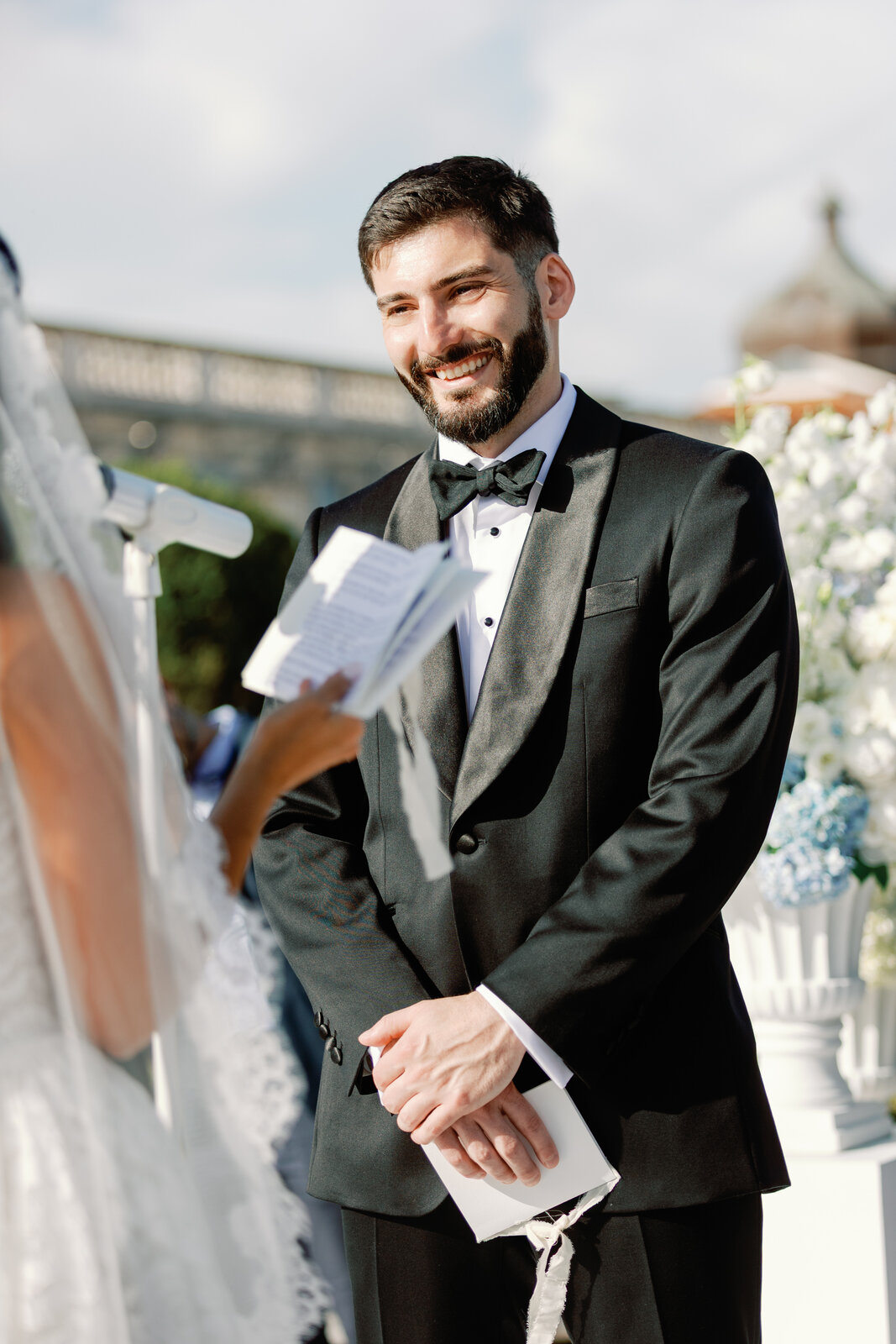 Groom smiling while holding his vow card during the ceremony