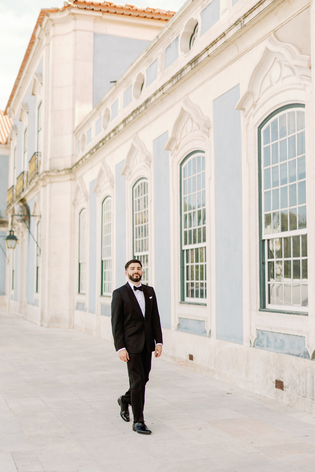 Groom portrait walking past the blue and white palace facade