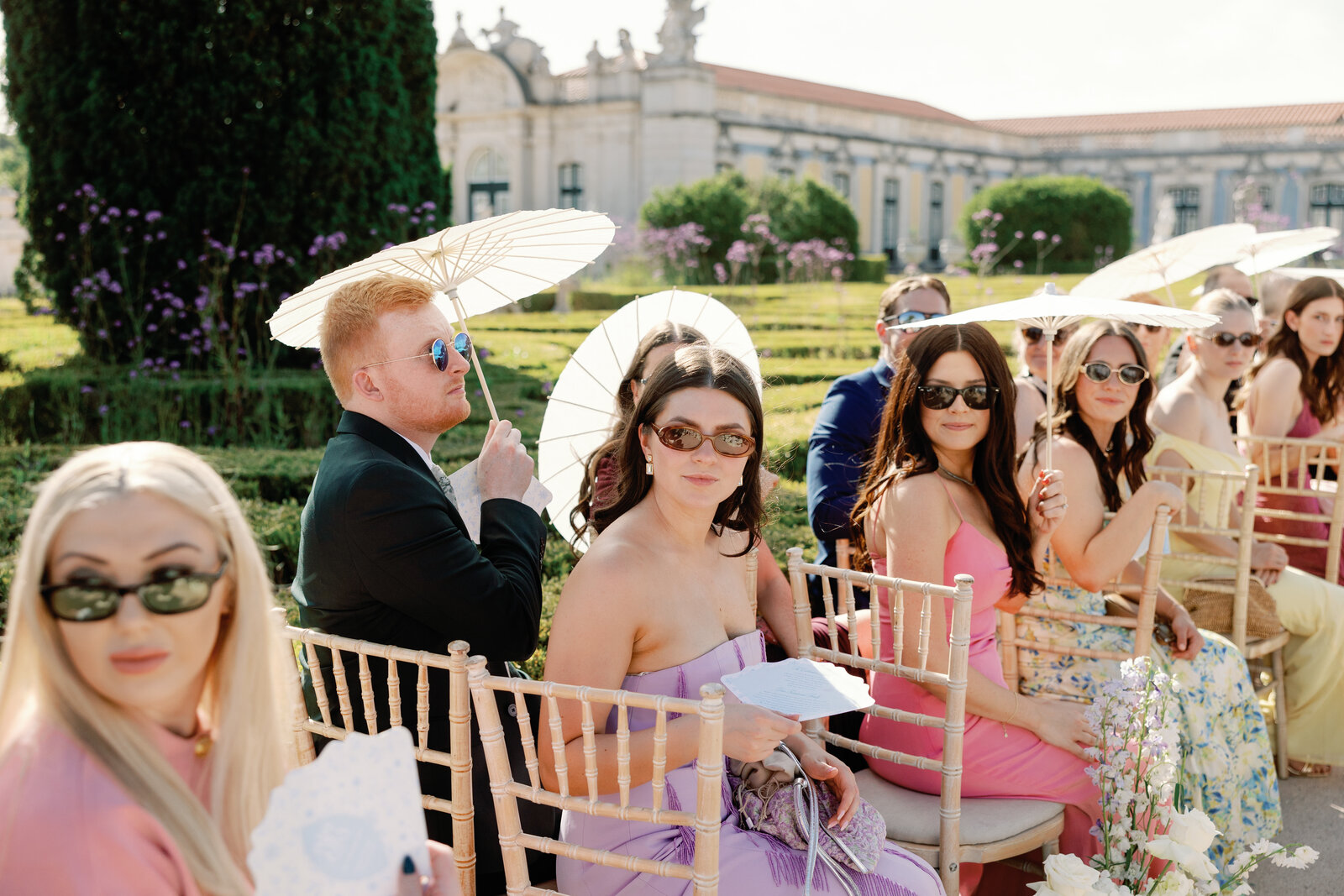 Guests in sunglasses and colorful dresses seated under umbrellas