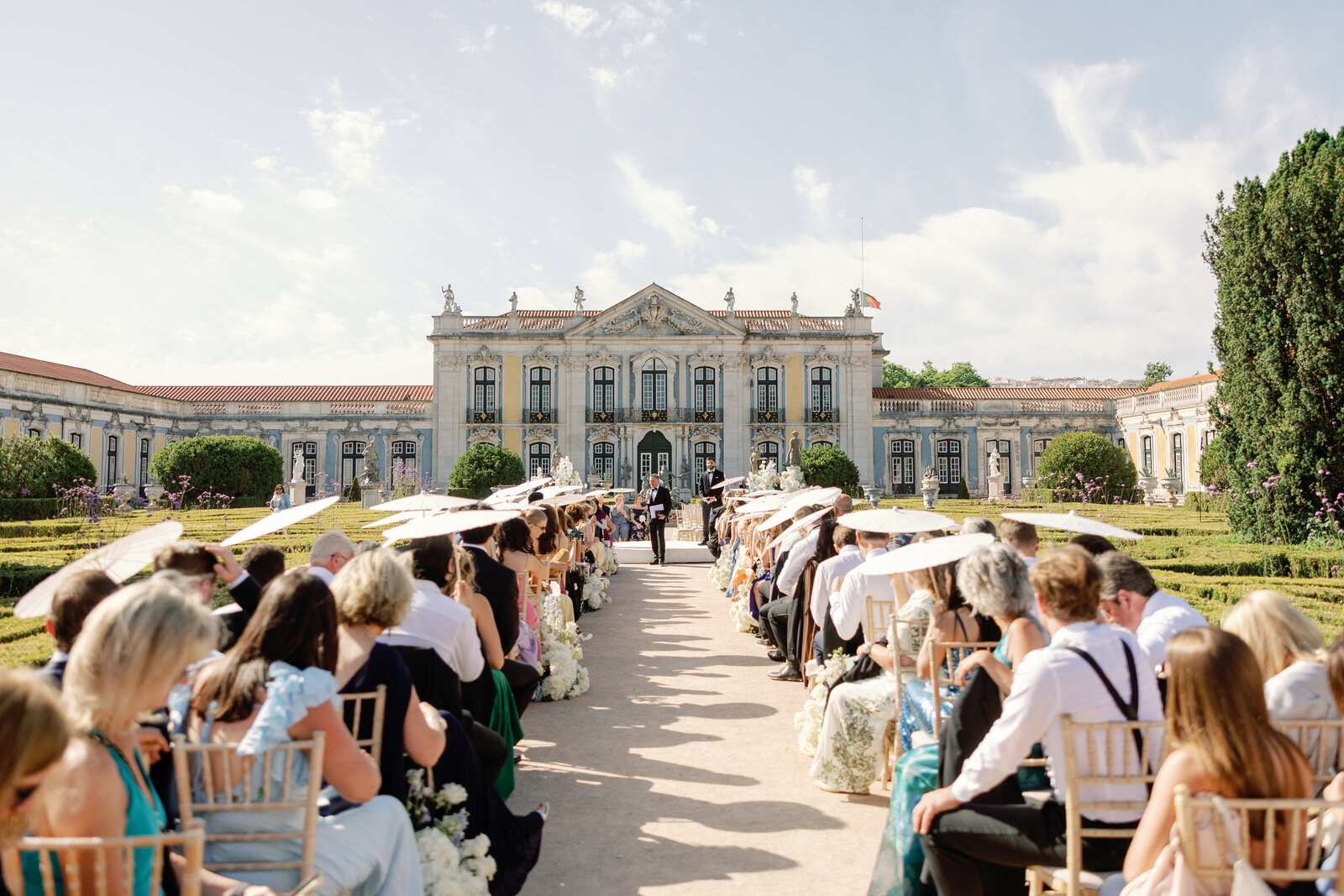 Wide view of guests seated with umbrellas facing the palace altar