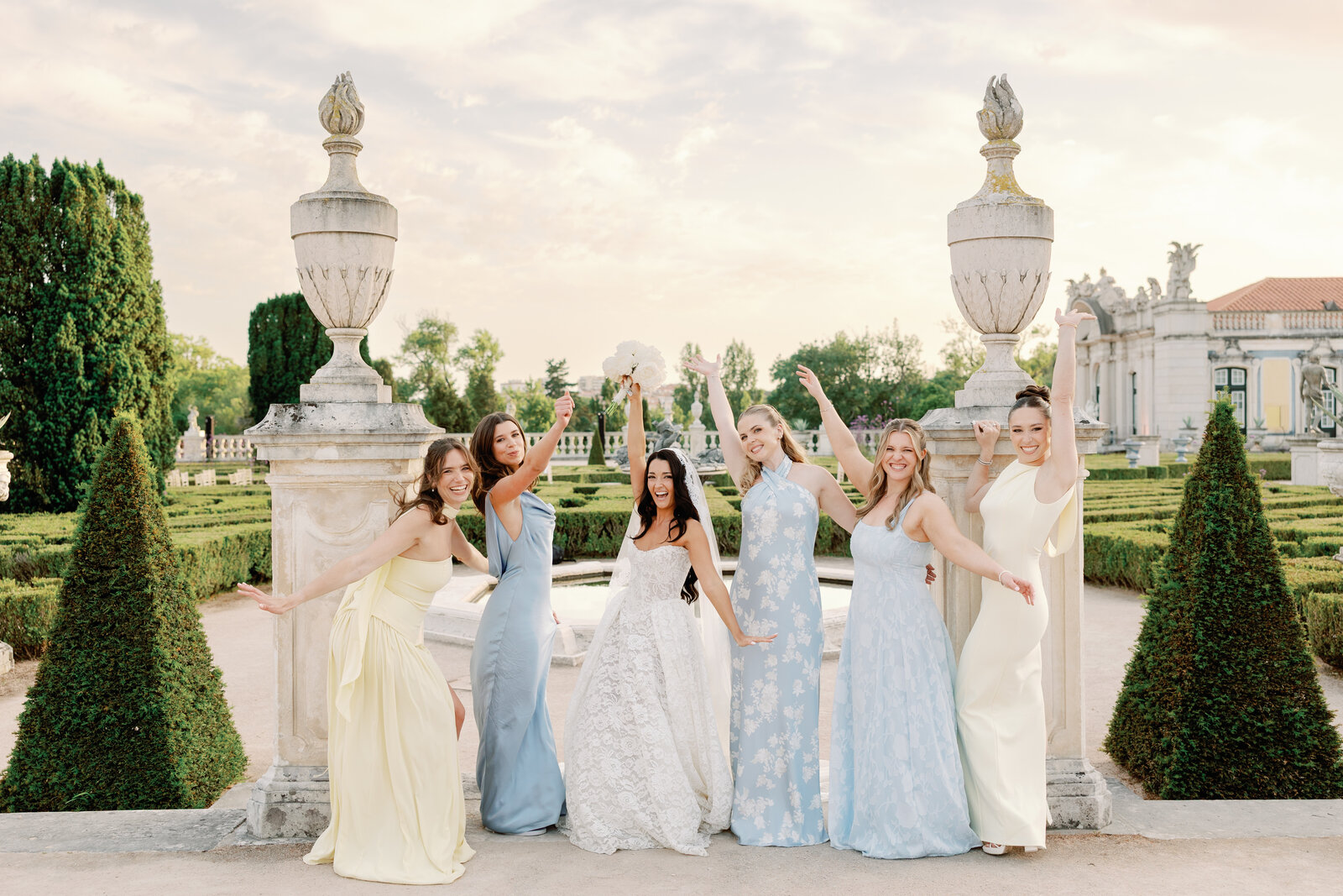 Bridal party cheering with arms raised beside garden urns
