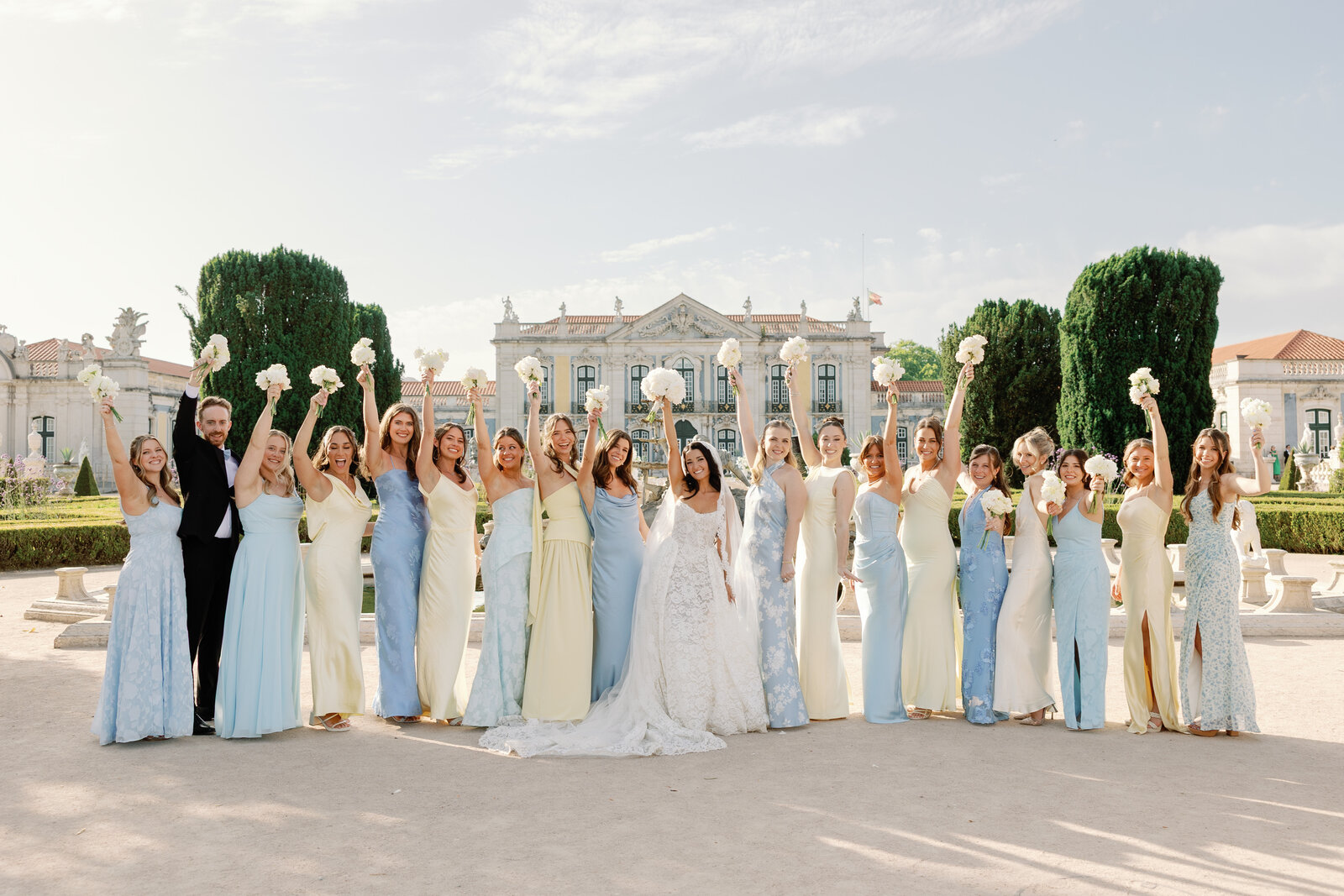 Bride and bridal party raising bouquets in front of the palace