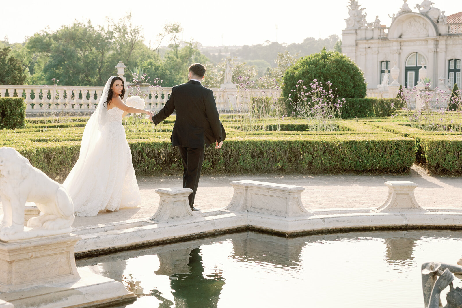 Bride and groom walking toward the boxwood hedge maze, bride looking back