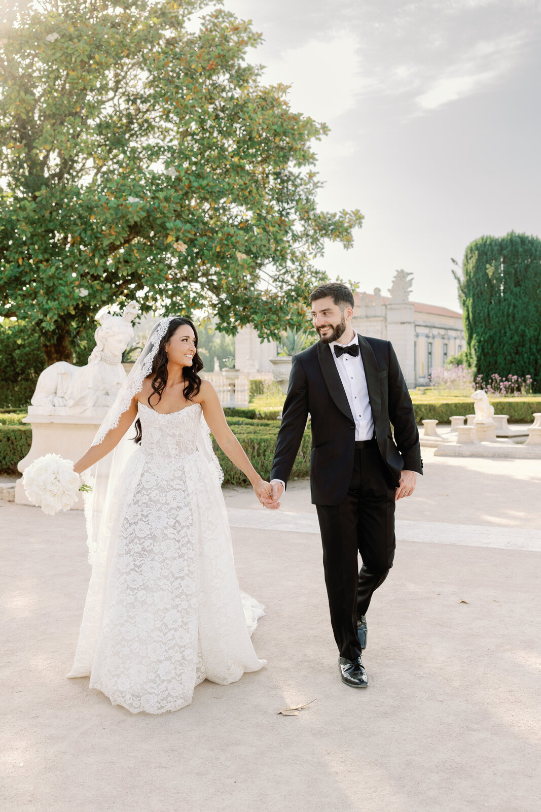 Bride and groom walking hand in hand past a garden statue