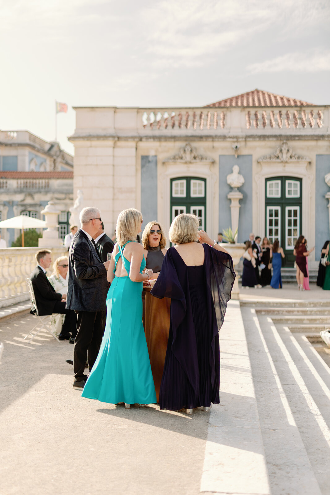 Guests in evening gowns chatting in front of the palace facade