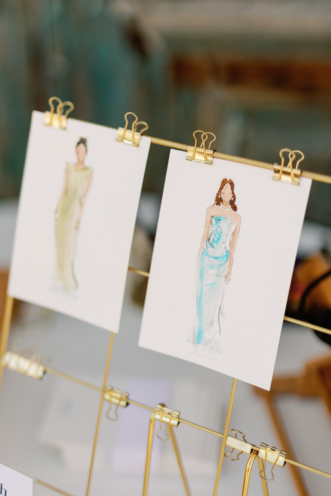 Live sketch portraits of guests in gowns clipped to a gold display rack