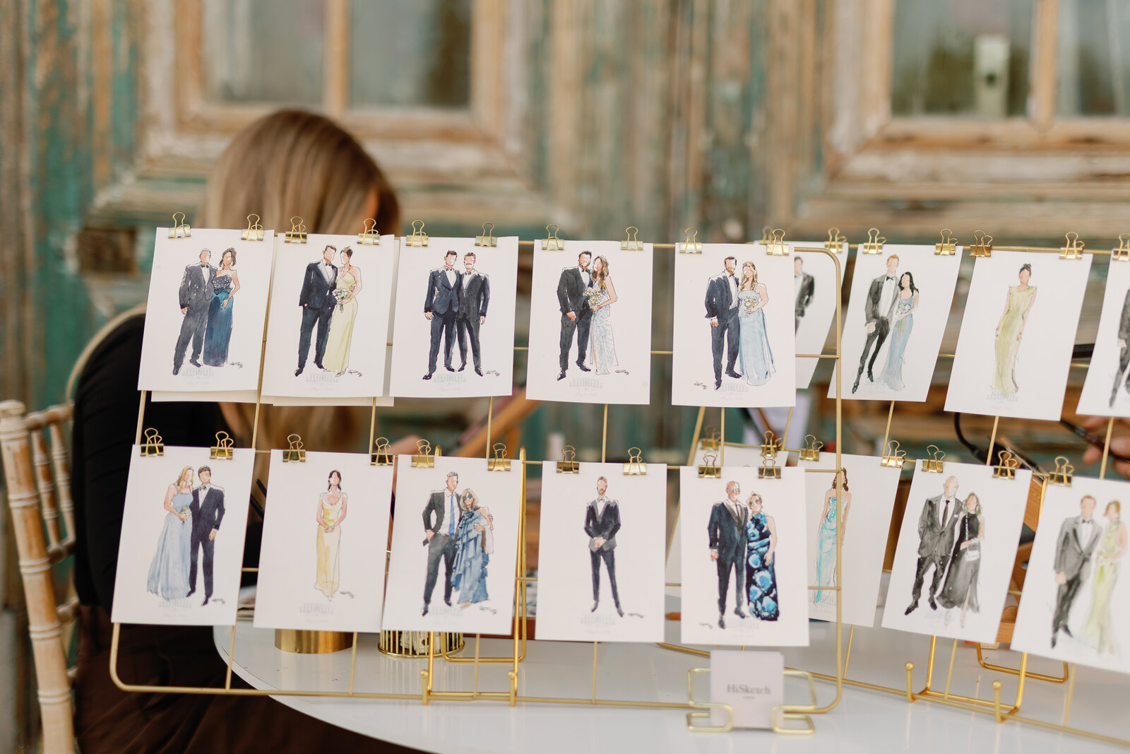 Rows of finished live sketch portraits clipped to a gold rack