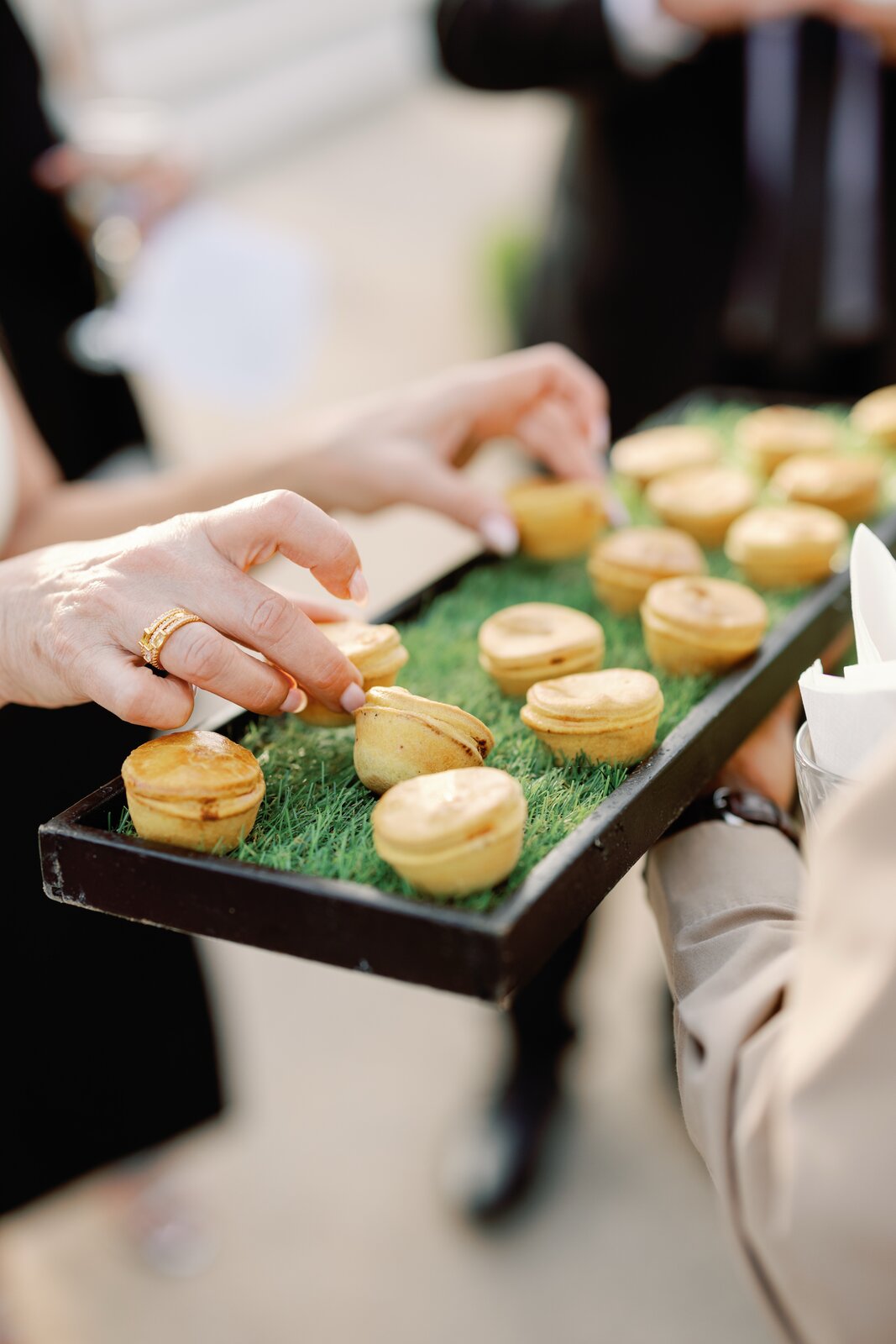 Guests taking mini savory pies from a grass-lined serving tray