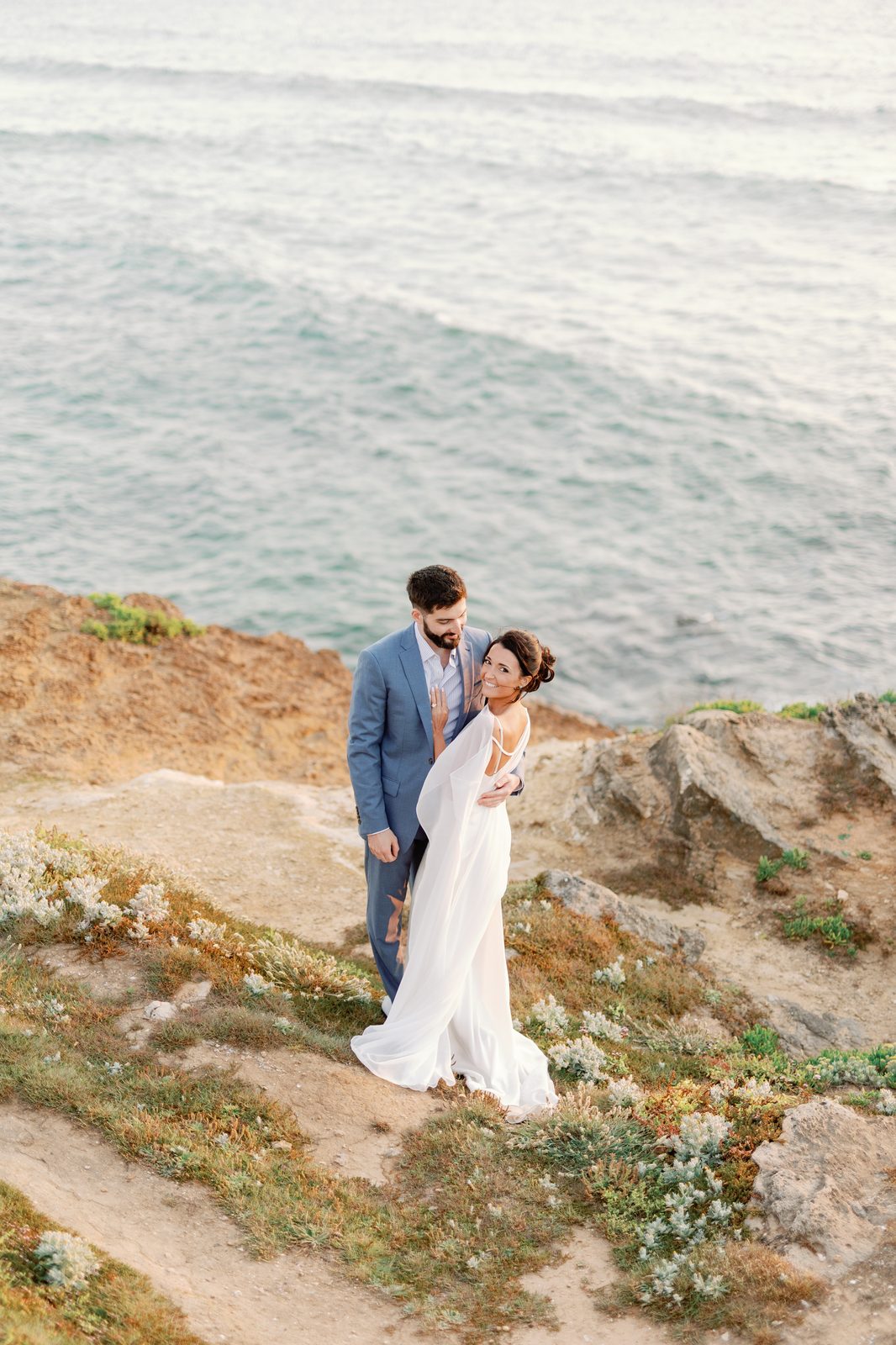 Bride and groom embracing on the cliffside overlooking the ocean