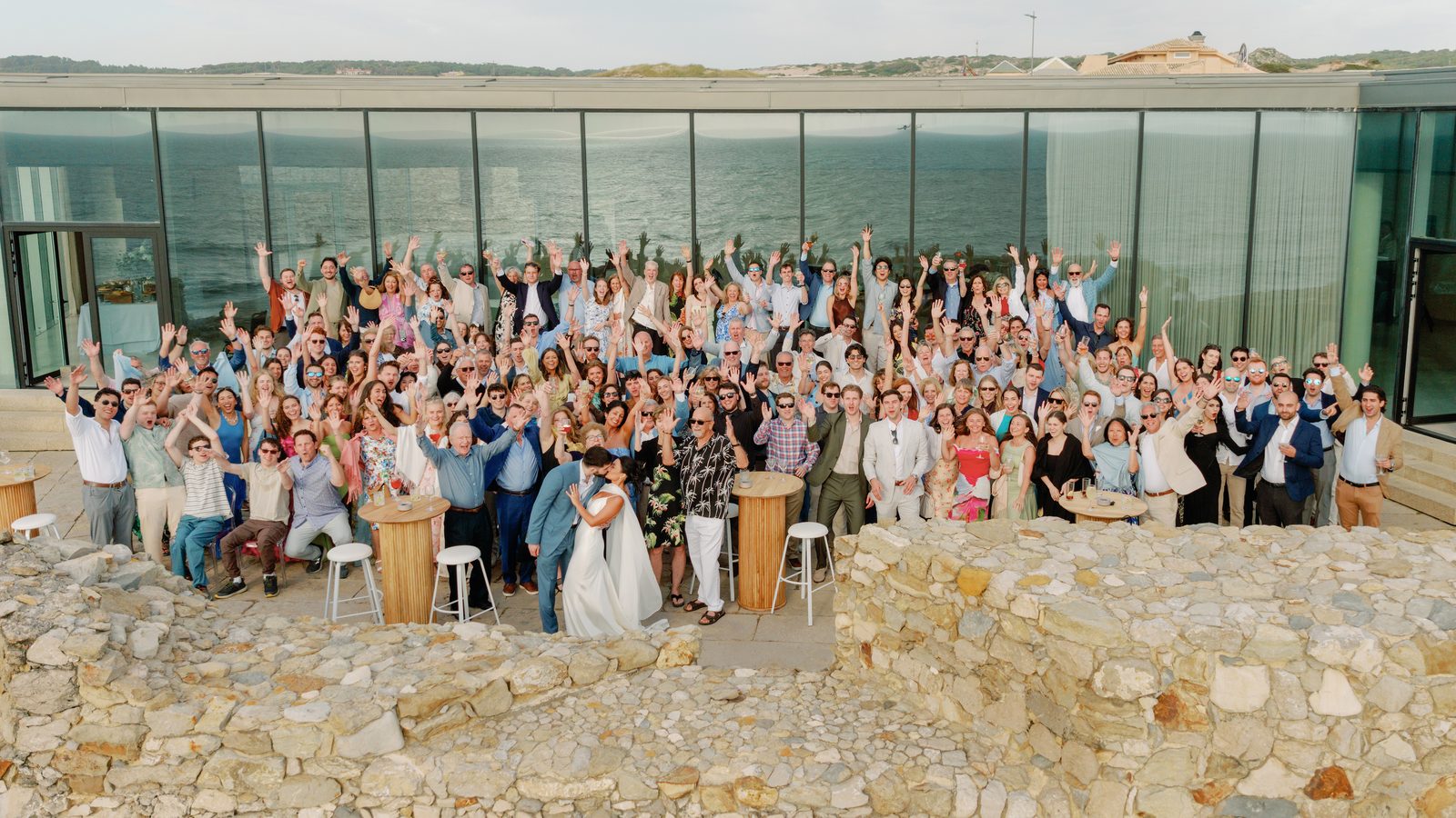 Full wedding party celebrating together with the ocean behind them