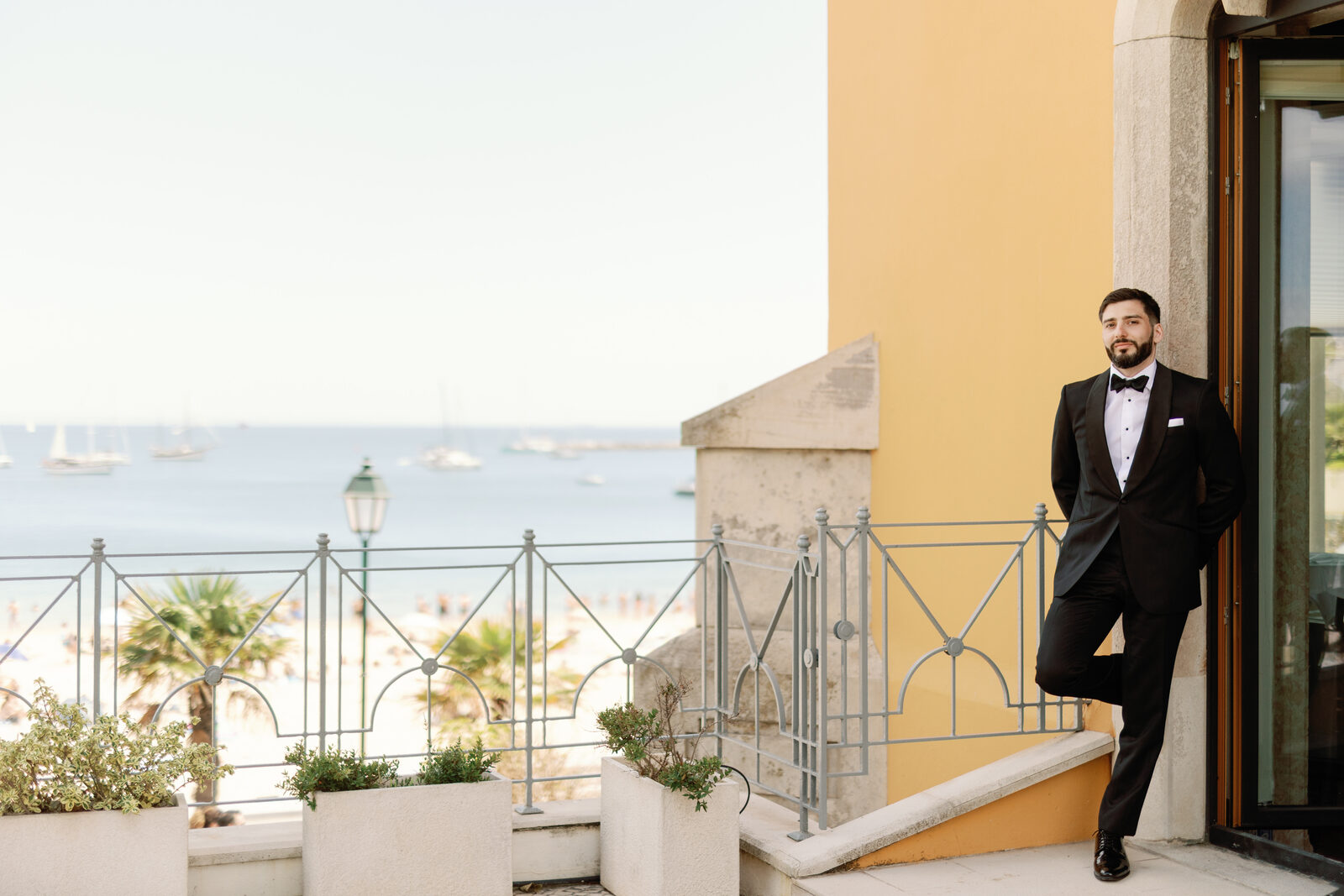 Groom leaning against a yellow wall overlooking the Cascais coastline
