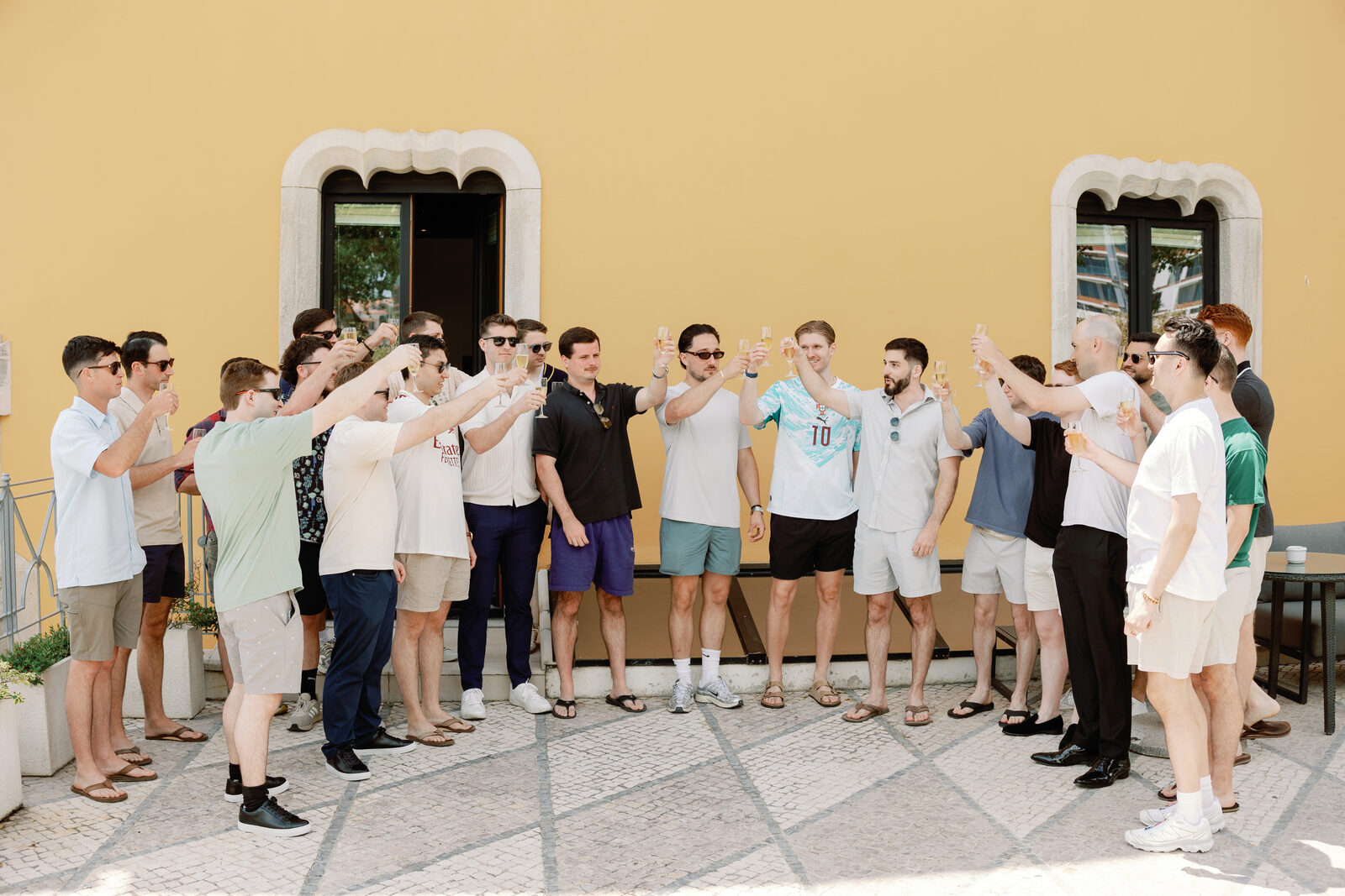 Groomsmen raising a champagne toast against a yellow courtyard wall