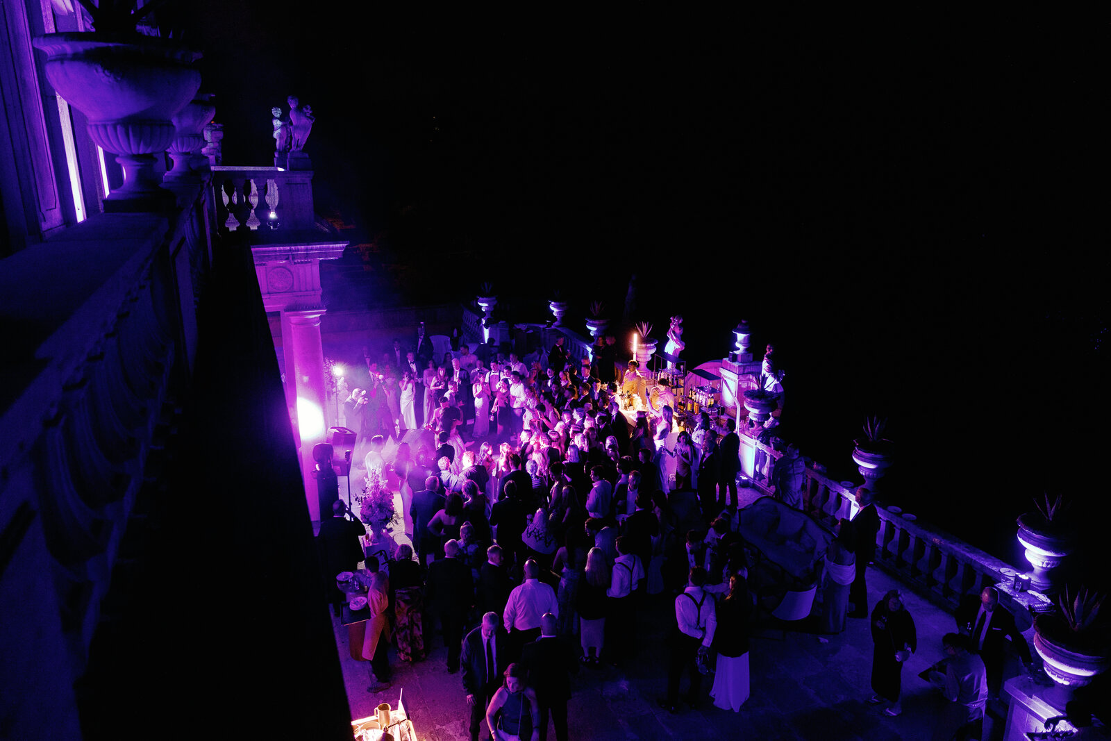 Aerial night view of guests gathered around the bar under purple lighting