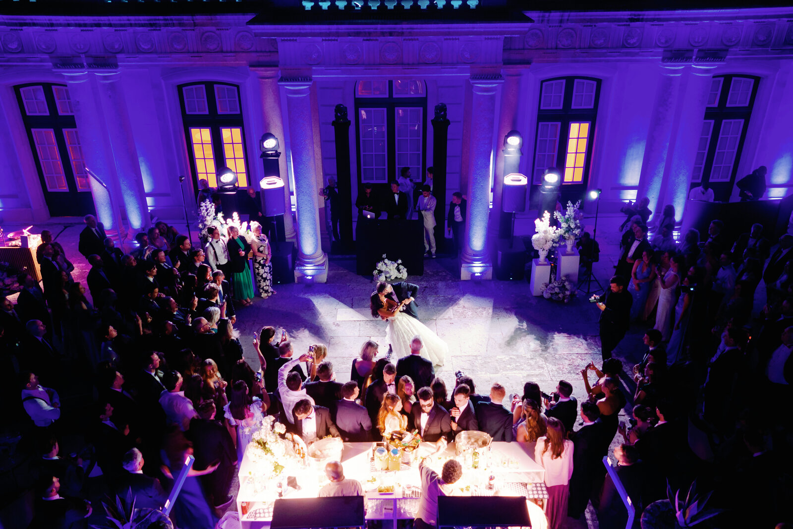 Aerial view of the bride and groom kissing in a dip surrounded by cheering guests