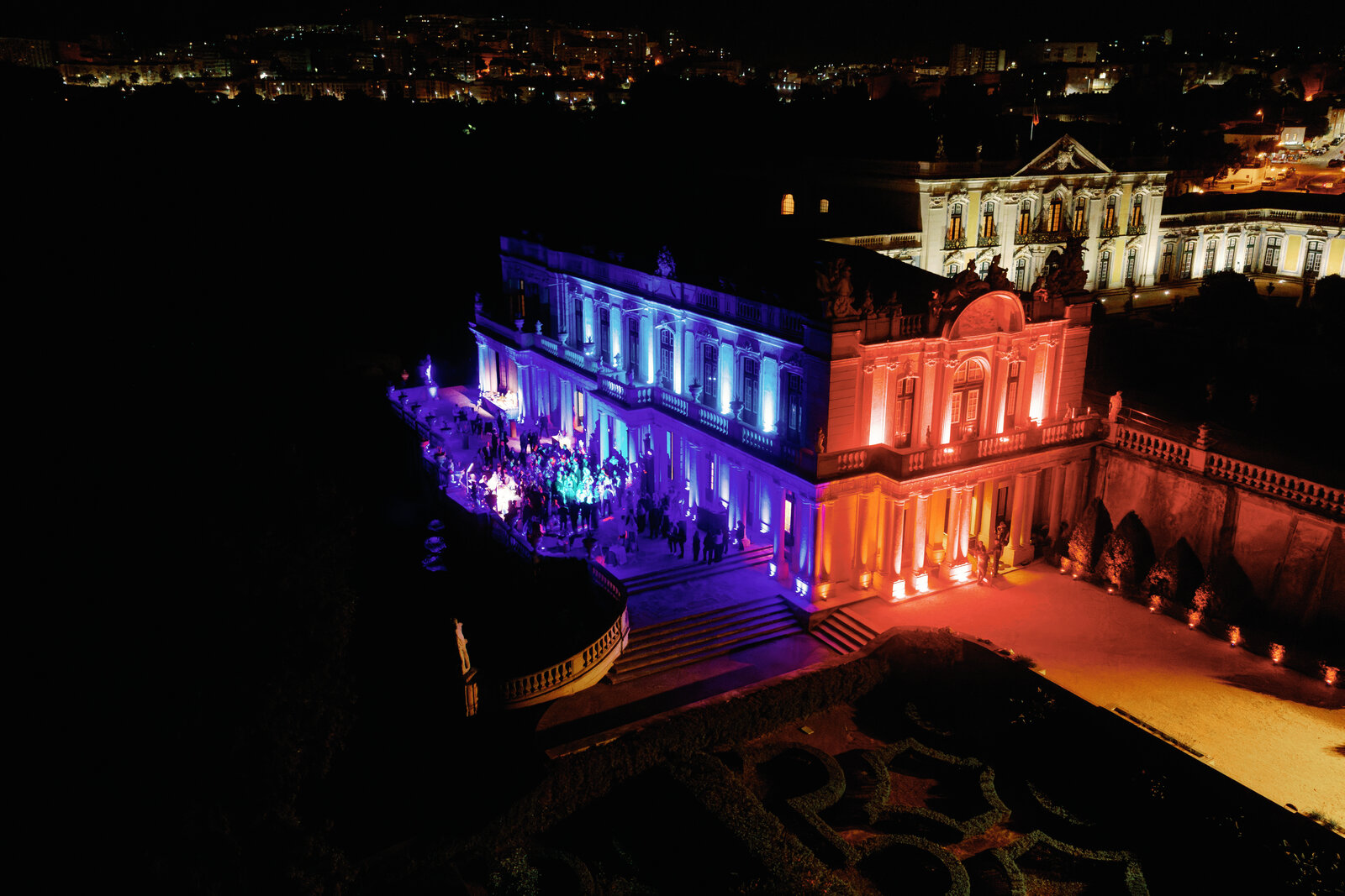 Aerial night view of the palace lit in blue and red with the city skyline beyond