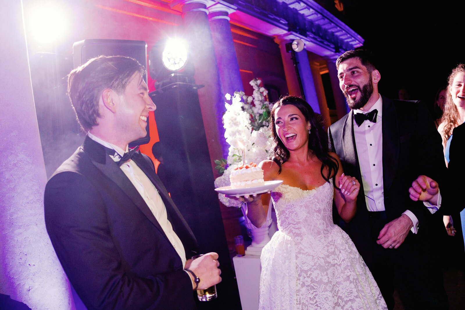 Bride and groom laughing over a slice of cake with a lit candle