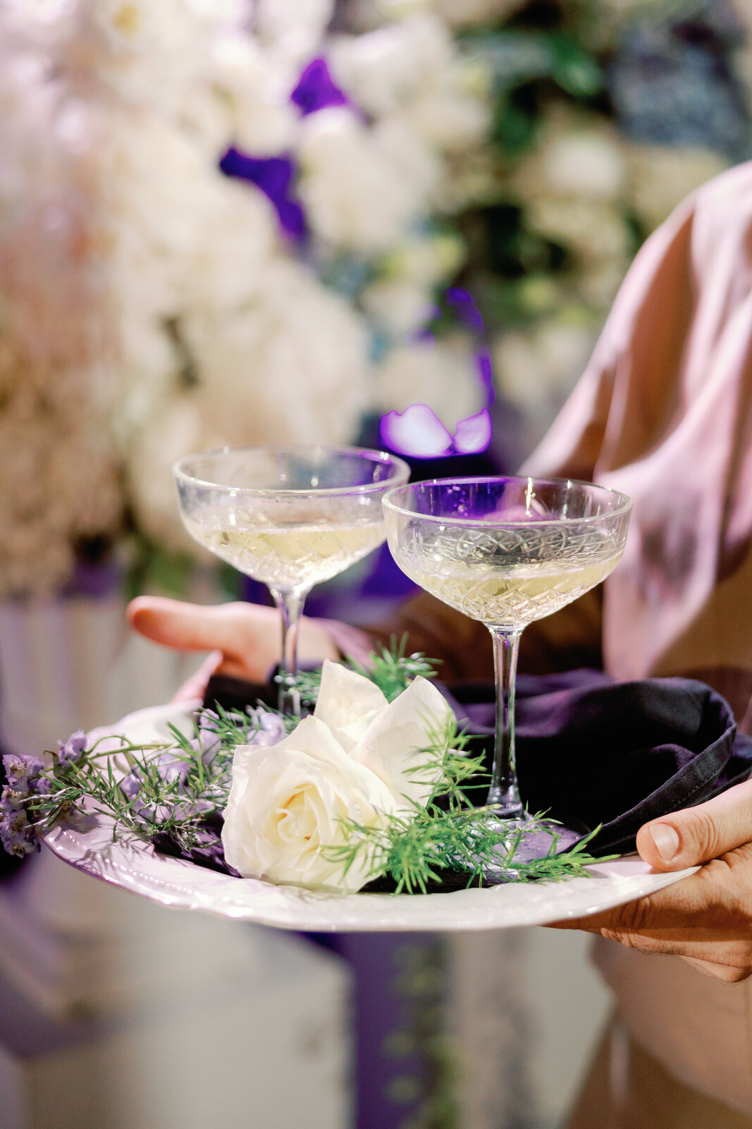 Two champagne coupes on a plate with a white rose garnish