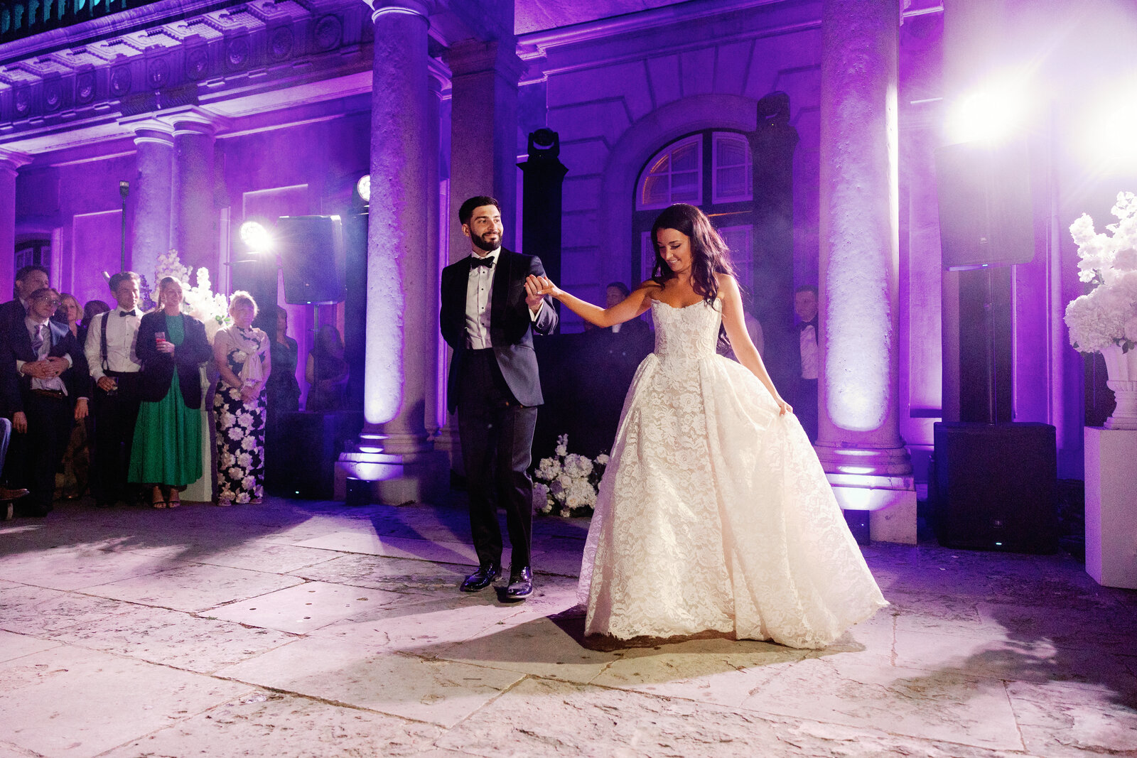Bride and groom holding hands while dancing beneath the palace columns