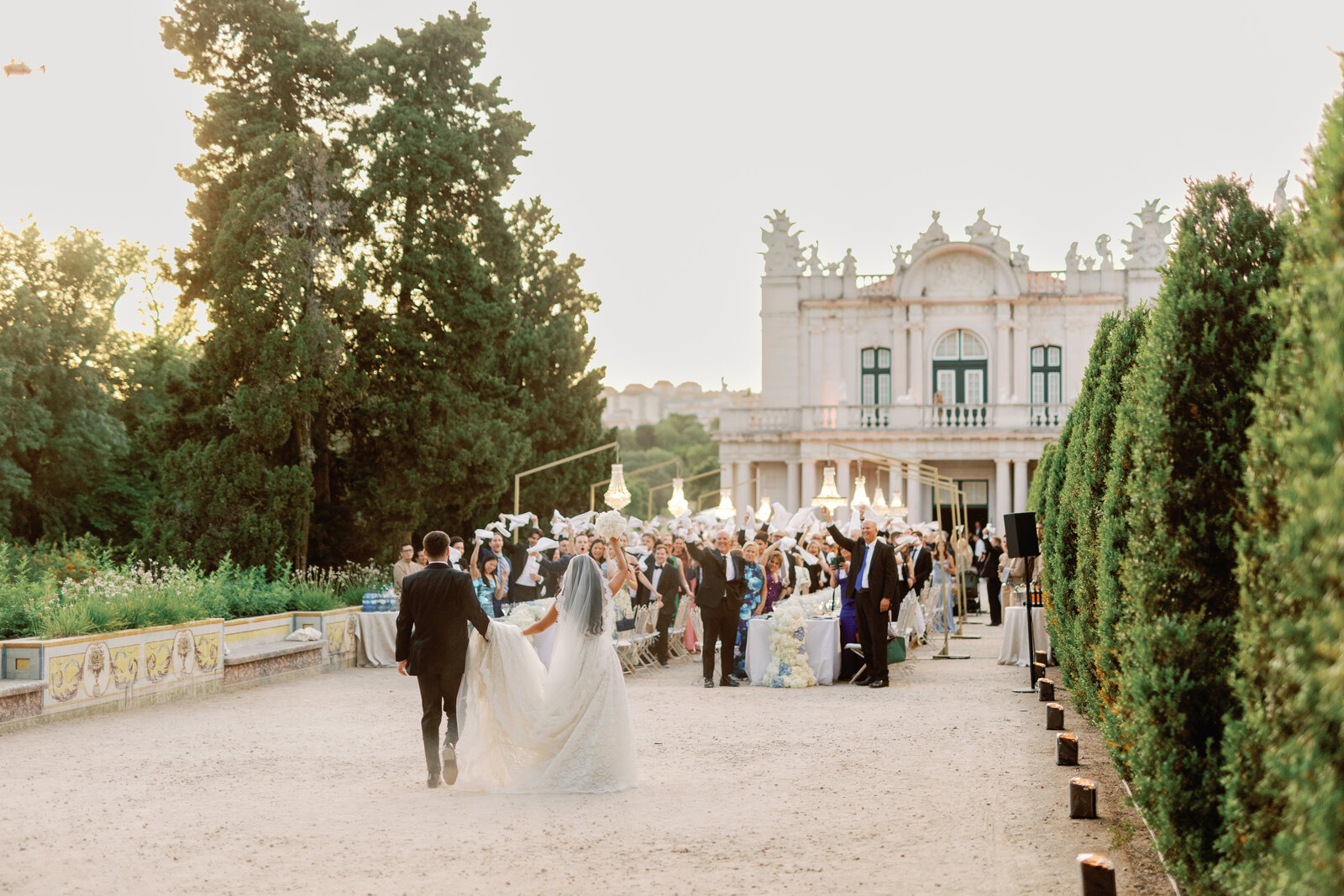 Bride and groom walking toward a cheering crowd waving napkins
