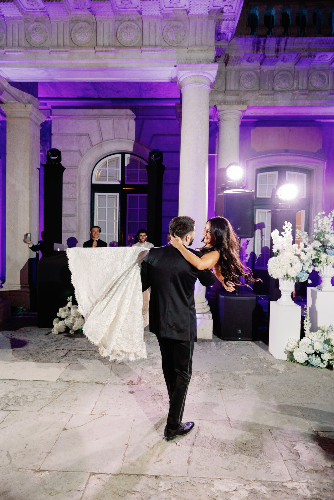 Groom carrying the bride with her lace dress draped over his shoulder